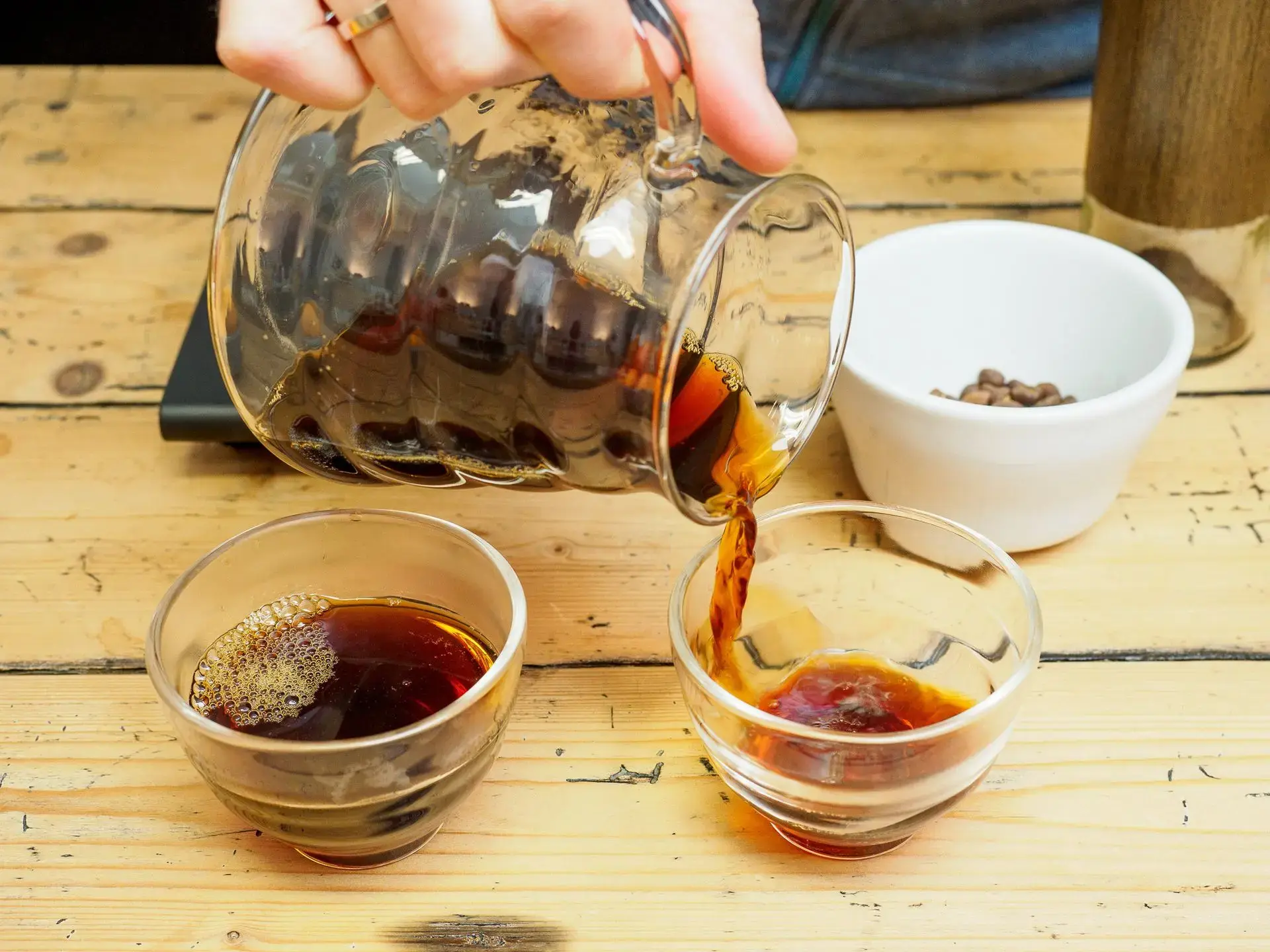 Frisch gebrühter Filterkaffee wird aus einer Hario Glaskaraffe in Tassen eingeschenkt, Spezialitätenkaffee von La Molienda Oldenburg.
